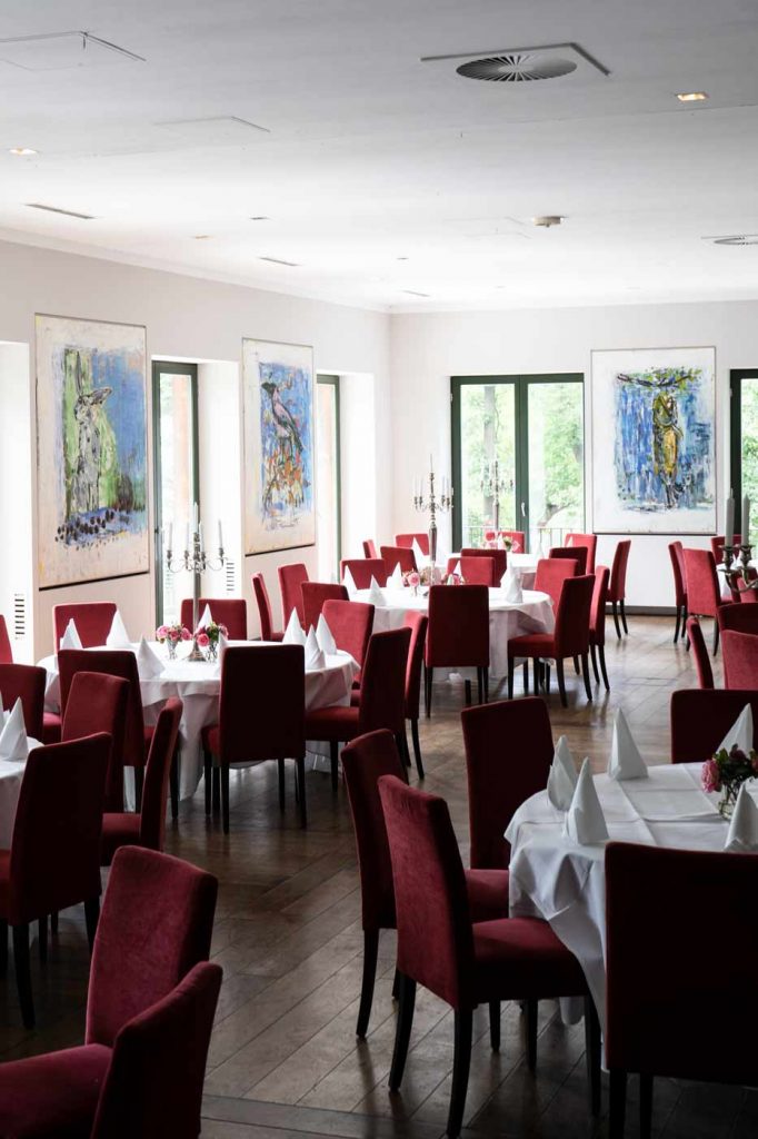 Heller Festsaal mit gedeckten Tischen und roten Stühlen für Hochzeiten, Feiern und Veranstaltungen.
