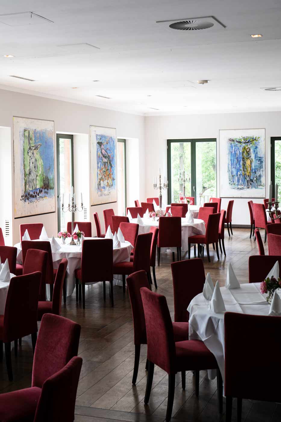 Moderner Festsaal mit runden Tischen, roter Bestuhlung und Kunst an den Wänden.