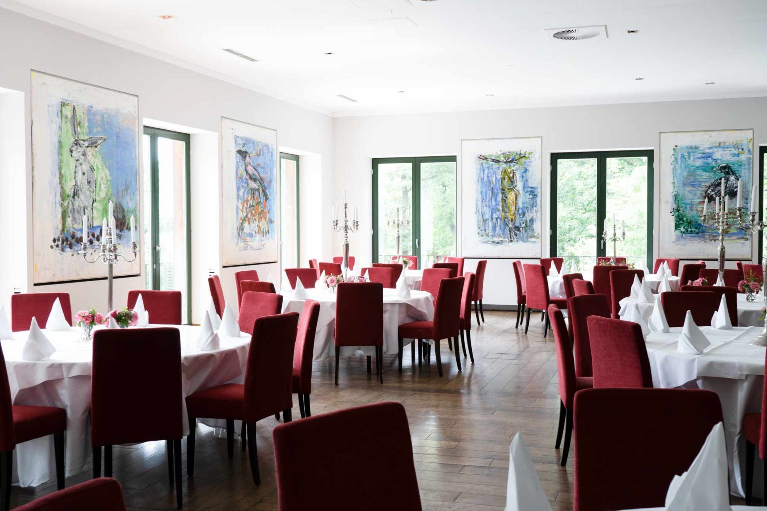 Heller Festsaal mit gedeckten Tischen und roten Stühlen für Hochzeiten, Feiern und Events.