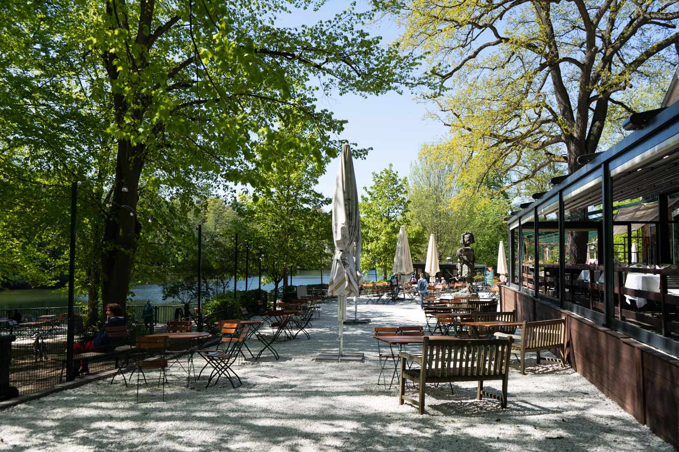 Seeterrasse mit Biergarten-Sitzplätzen, Bäumen und Blick auf das Wasser.