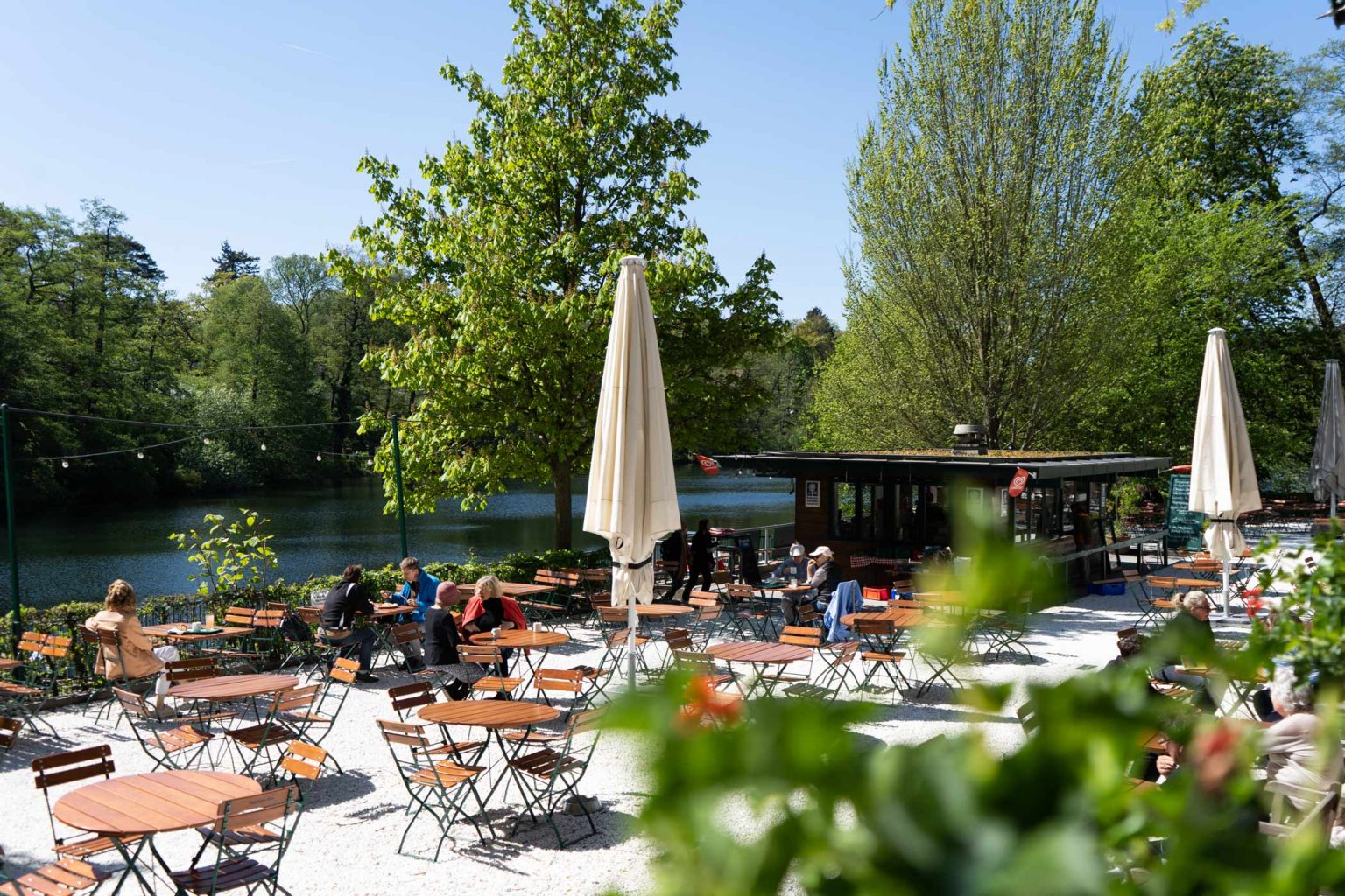 Biergarten am See mit Sonnenschirmen, Holztischen und gemütlichem Außenbereich.