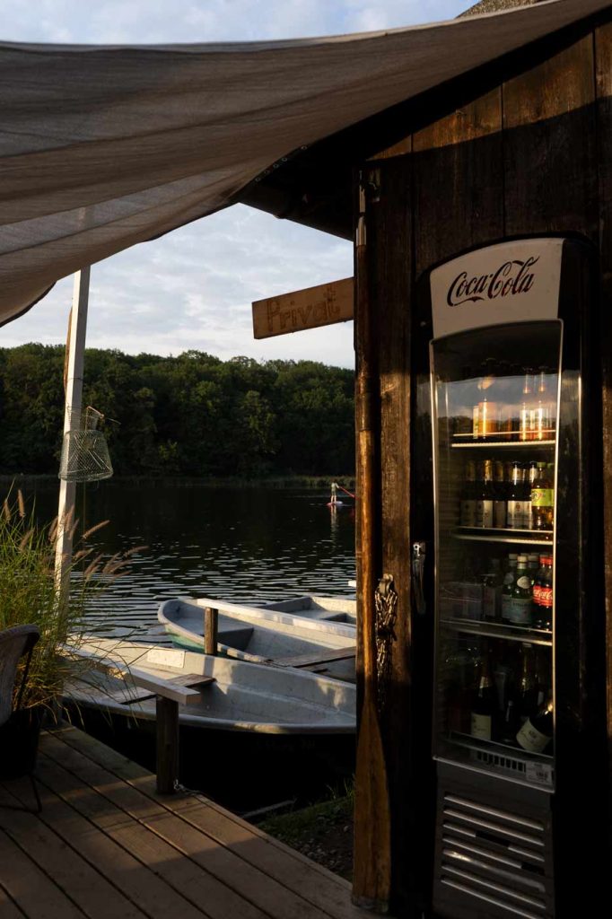 Bootsverleih am See mit Bootssteg, Ruderboot und Getränkeautomat in natürlicher Umgebung.