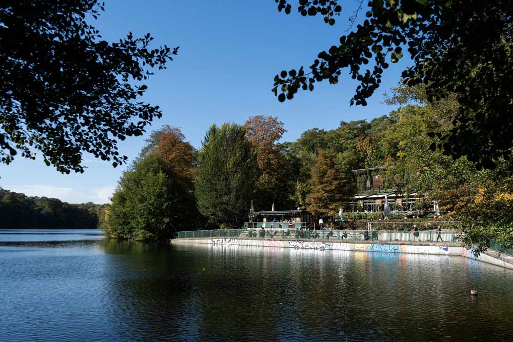 Blick über den See auf den Biergarten mit Terrasse und Bootssteg.