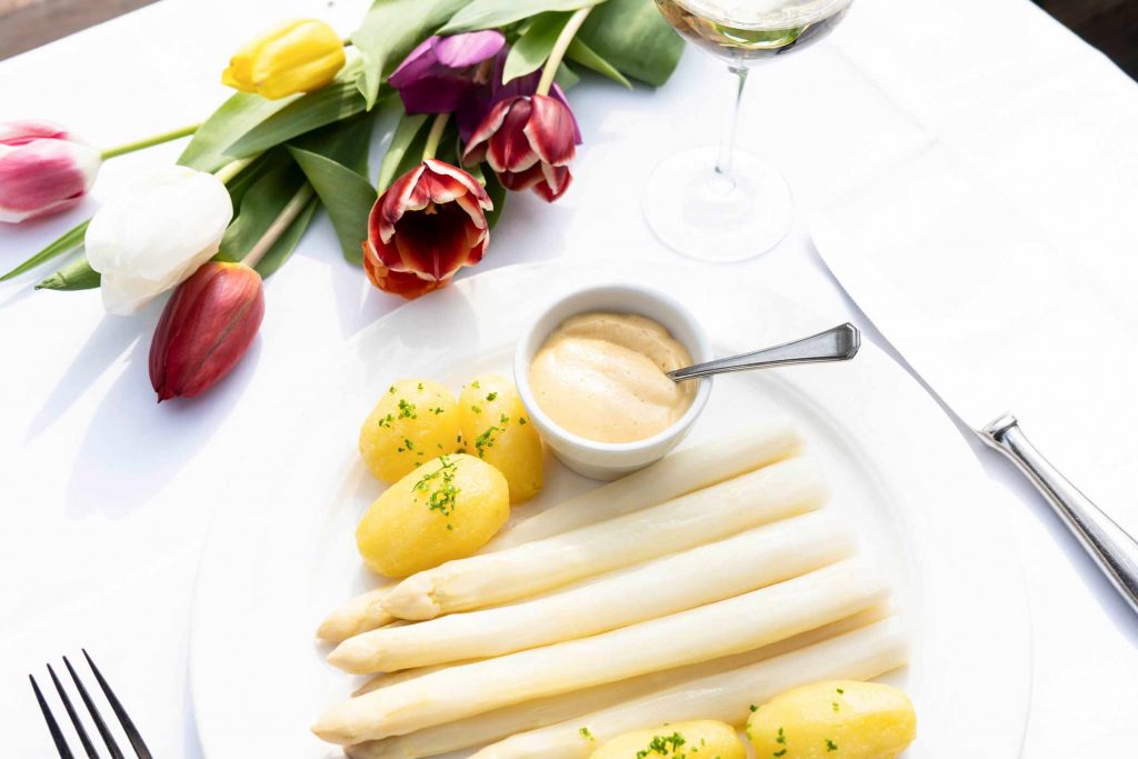 Spargelgericht mit Kartoffeln und Sauce Hollandaise auf weiß gedecktem Tisch.