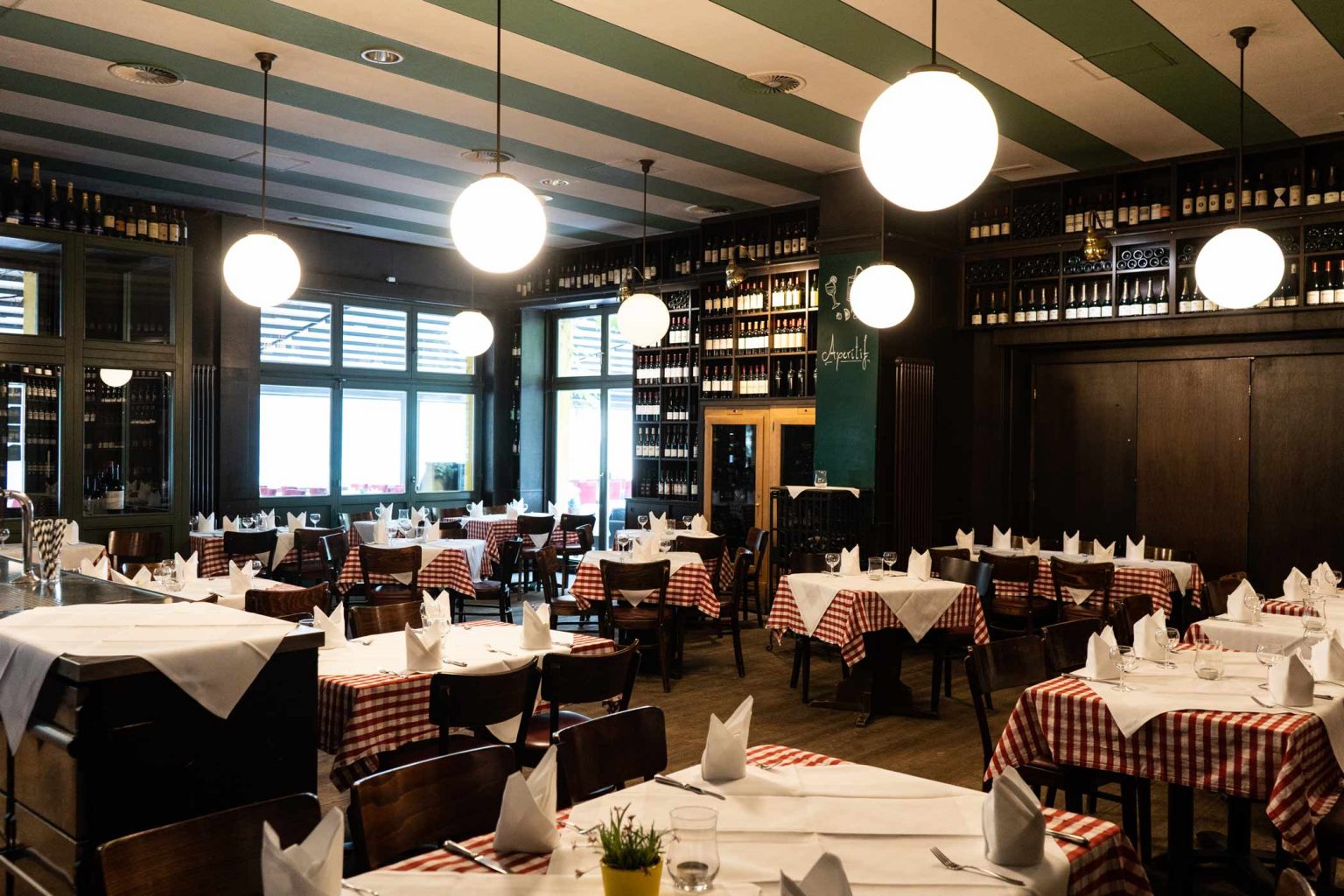 Restaurant mit langen gedeckten Tafeln, Weinregalen und warmem Licht für Veranstaltungen.