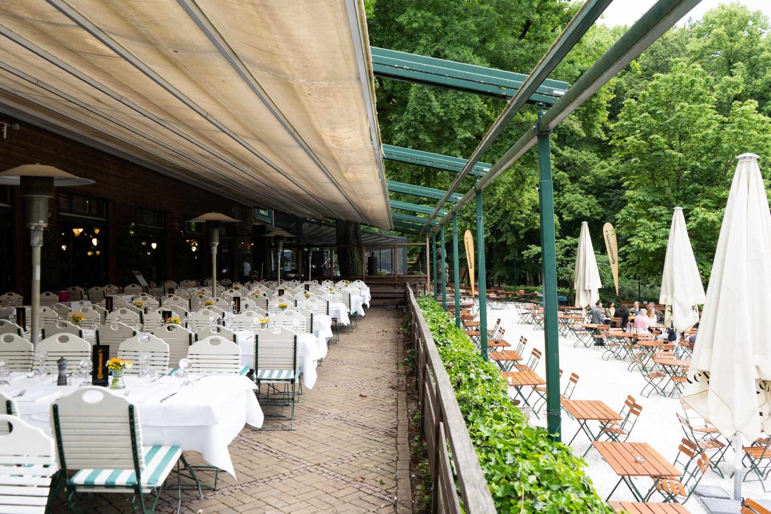 Wirtshaus-Terrasse mit gedeckten Tischen, Markise und grünem Außenbereich.