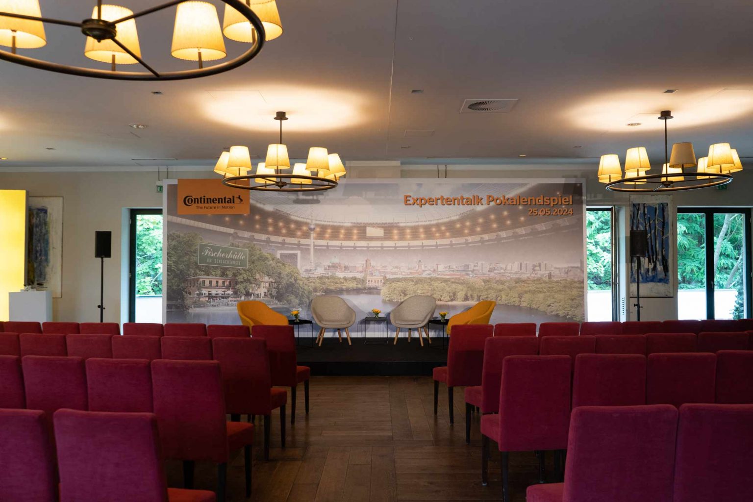 Moderner Festsaal mit roten Stühlen, Bühne und Technik für Firmenveranstaltungen.