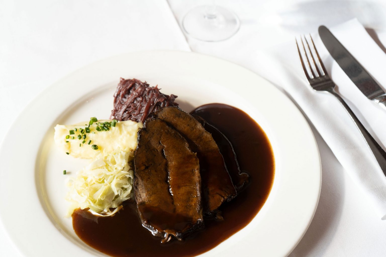 Wirtshausgericht mit Fleisch, Kartoffelstampf und kräftiger Sauce auf weißem Teller.