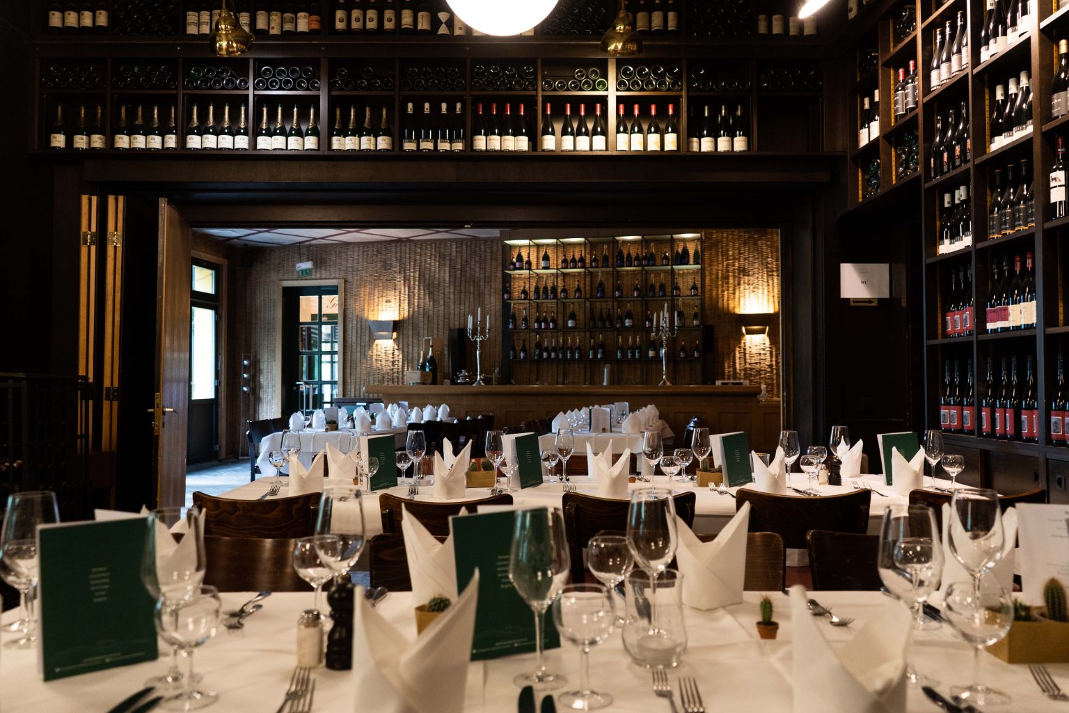 Stilvoller Veranstaltungsraum mit Bar, gedeckten Tischen und Weinregalen.