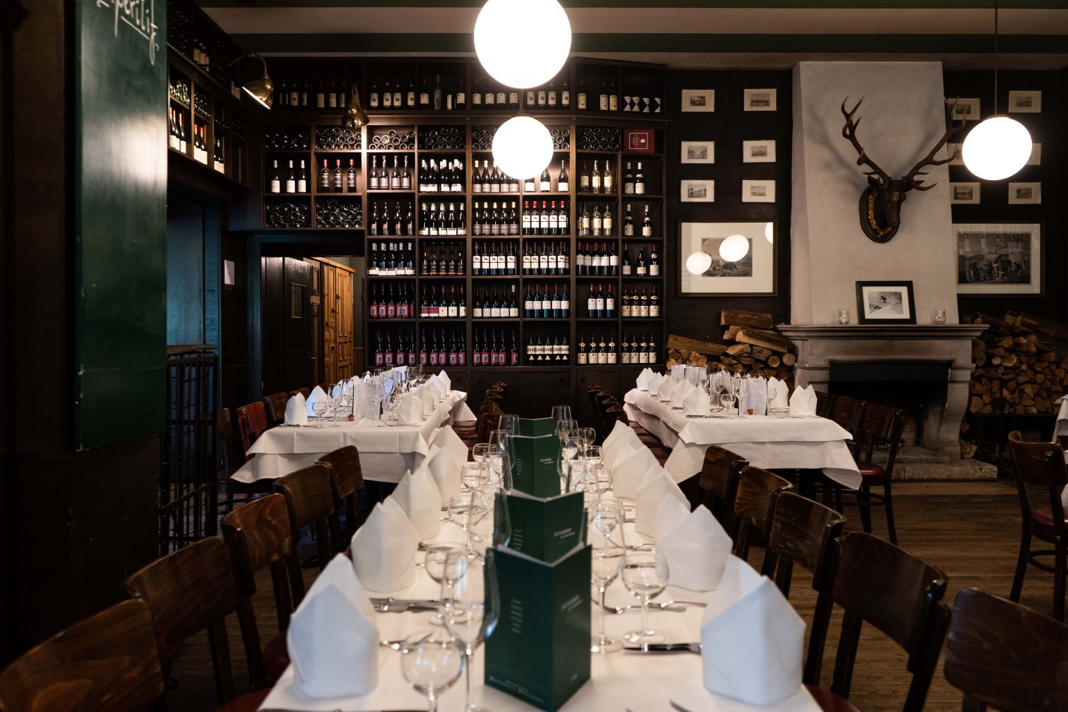 Festlich gedeckte Tafel mit Menükarten, weißen Servietten und Weinregalen im Hintergrund.