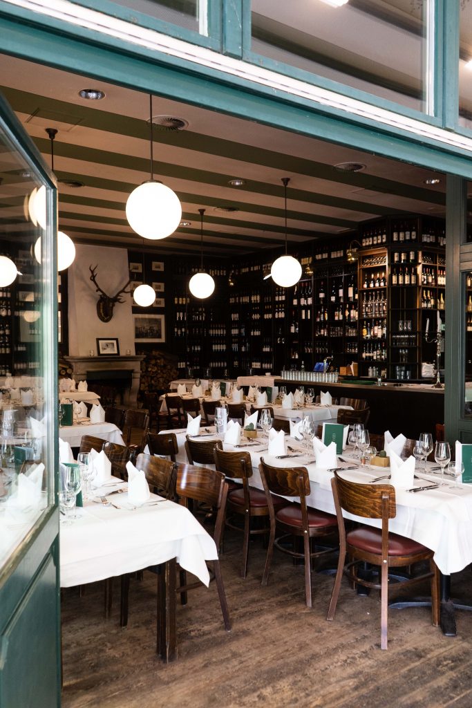 Stilvoller Restaurantbereich mit gedeckten Tischen, Weinregalen und Bar für Feiern und Events.
