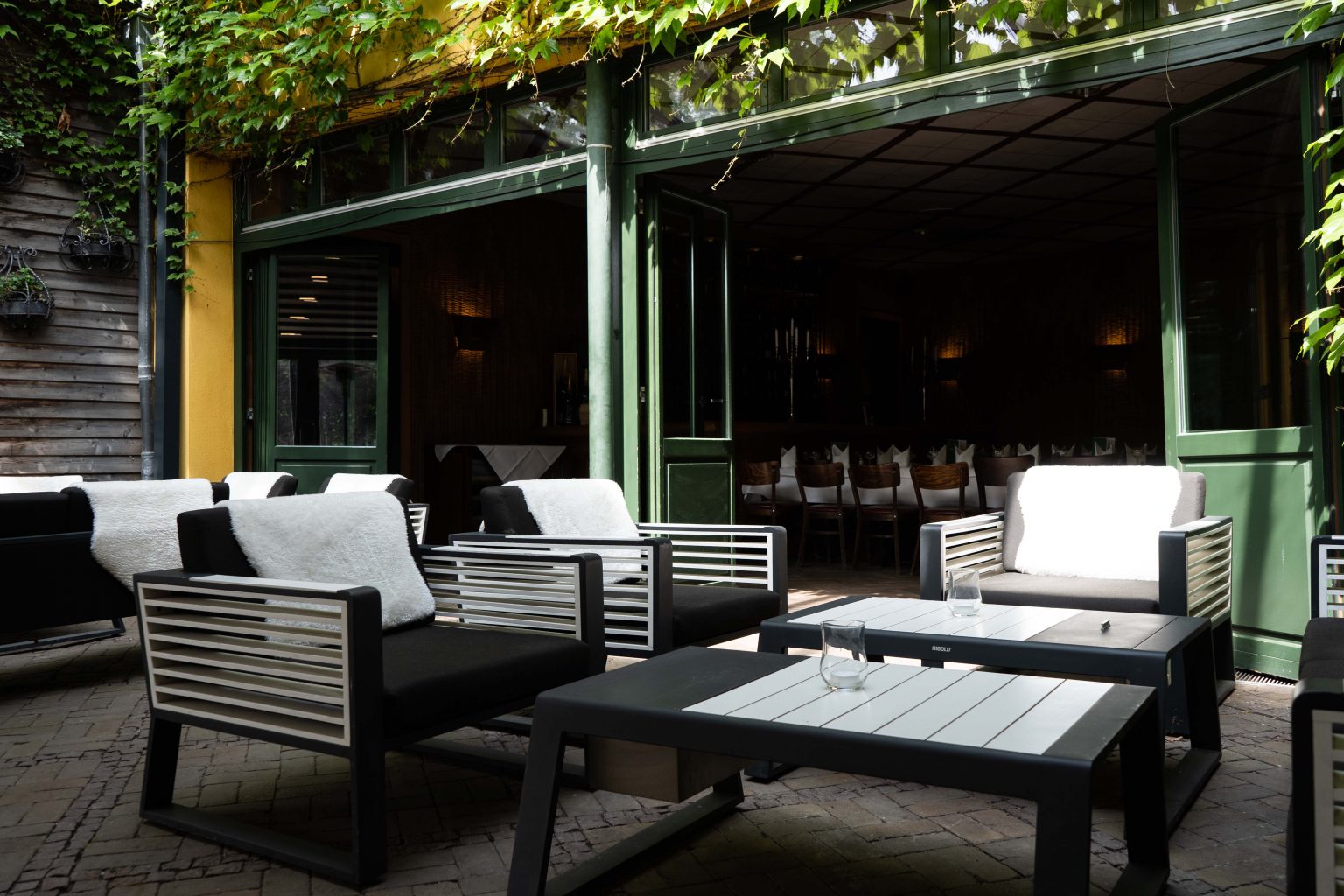 Überdachte Lounge-Terrasse mit modernen Sitzmöbeln und grünem Ambiente.
