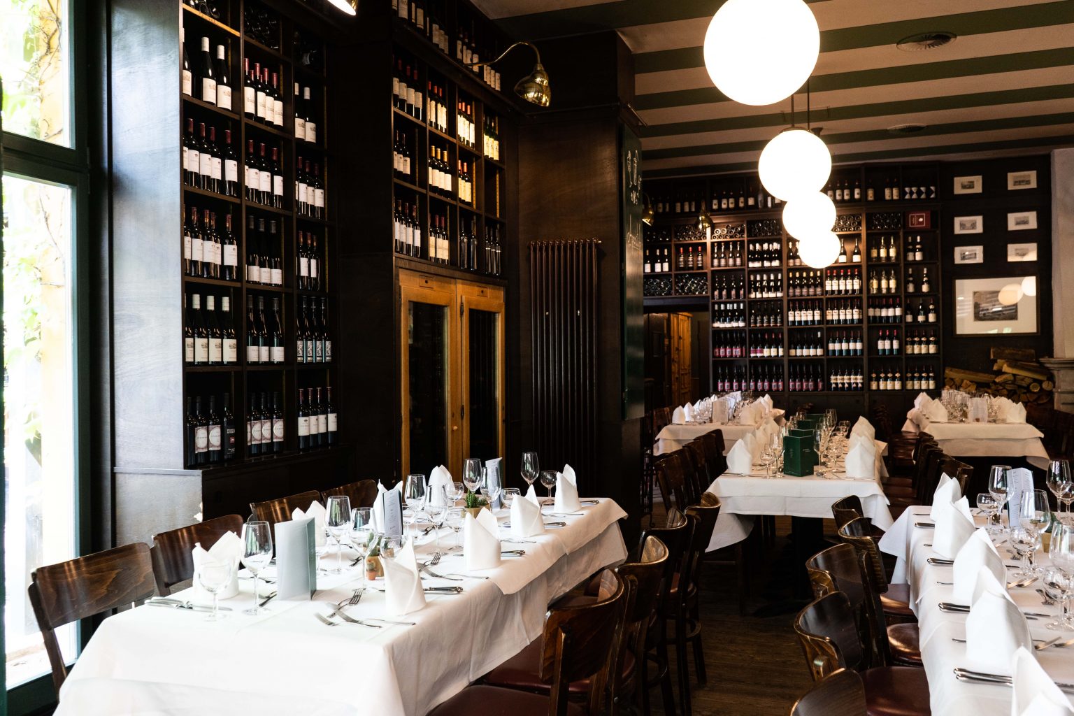 Restaurantbereich mit gedeckten Tischen, Holzstühlen und Weinregalen für Events.