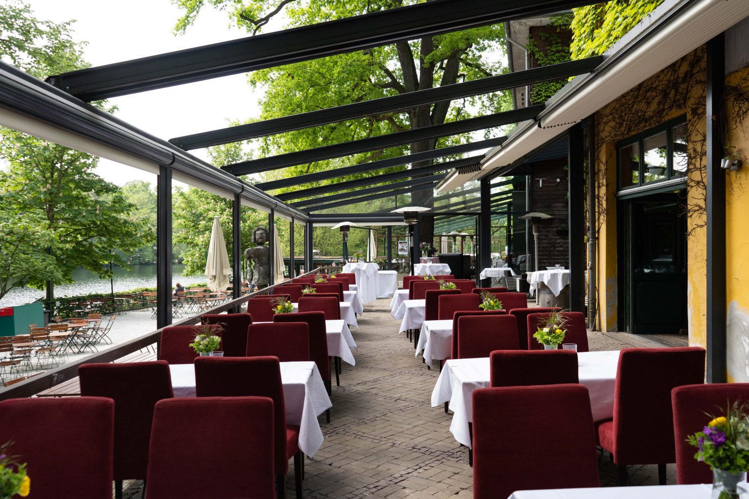 Terrasse mit gedeckten Tischen und roten Stühlen für Feiern und Events im Grünen.