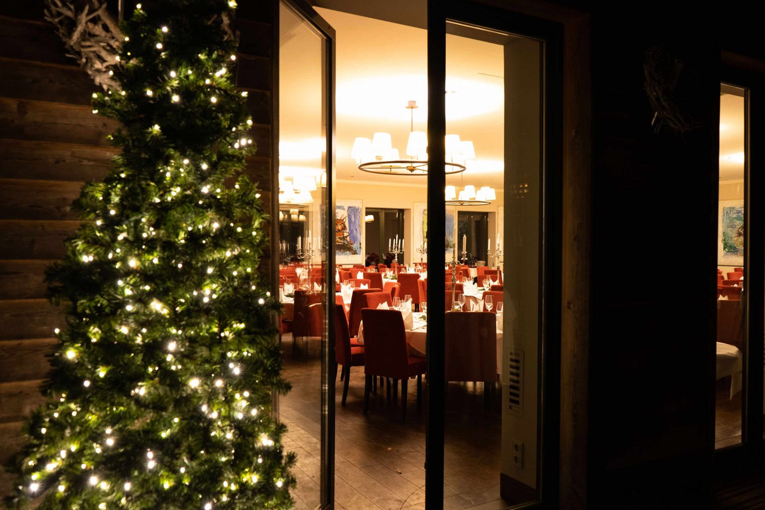 Festlich beleuchteter Eingang zum Festsaal mit Weihnachtsbaum und Abendambiente.